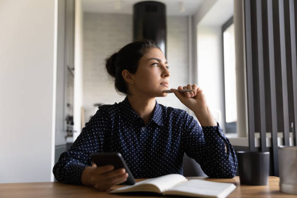 istock Pensive Indian woman make notes working on smartphone 1300836737