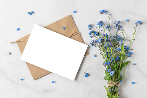 Blank greeting card with forget me not flowers bouquet on white background with copy space. top view. mock up. flat lay. wedding or holiday concept. festive background