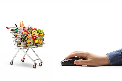 Male hand with a computer mouse and a shopping cart with food isolated on white background
