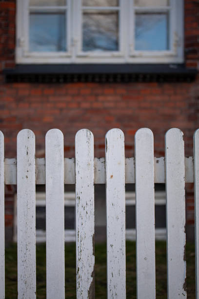 istock Weathered white fence with blurred building 1300841059