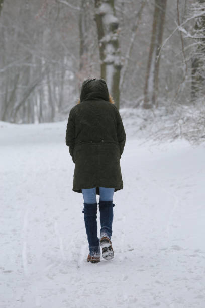 istock Blurred view on back of one unrecognizable woman walking alone on snow covered path in lonely german forest with bare trees during snowstorm in winter 1300841724