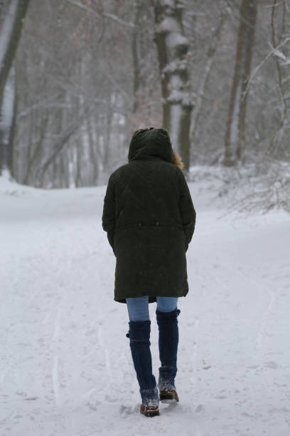 istock Blurred view on back of one unrecognizable woman walking alone on snow covered path in lonely german forest with bare trees during snowstorm in winter 1300842374