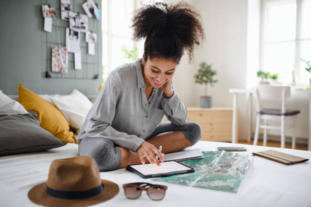 Young woman with tablet and map indoors at home, planning traveling trip. Happy young woman with tablet and map indoors at home, planning traveling trip. planning stock pictures, royalty-free photos & images