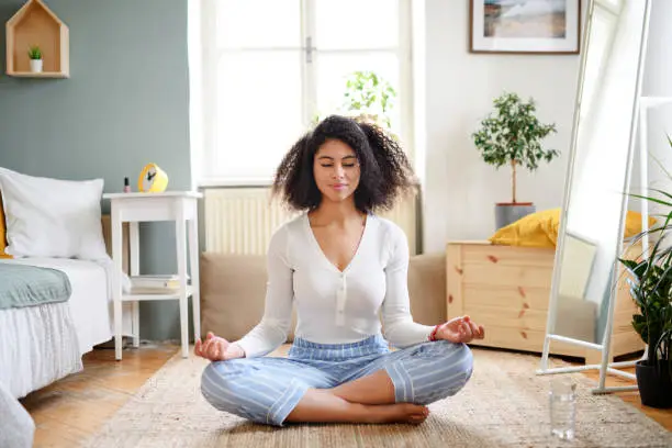 Portrait of relaxed young woman indoors at home, doing yoga exercise.