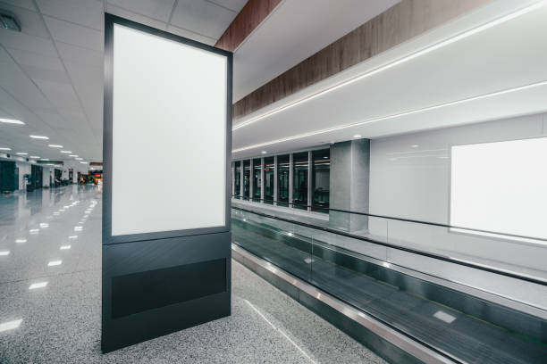 Travelator and a blank poster mockup Wide-angle view of a vertical empty advertising billboard mockup next to the travelator indoors of a modern airport; a template of a blank information poster in the railroad terminal, moving walkway airport travelator stock pictures, royalty-free photos & images