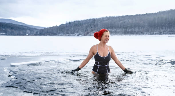 vista frontale della donna anziana attiva in costume da bagno all'aperto in acqua in inverno, concetto di terapia del freddo. - brina acqua ghiacciata foto e immagini stock