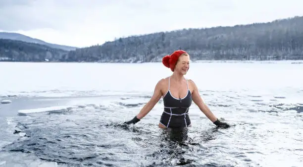 Photo of Front view of active senior woman in swimsuit outdoors in water in winter, cold therapy concept.