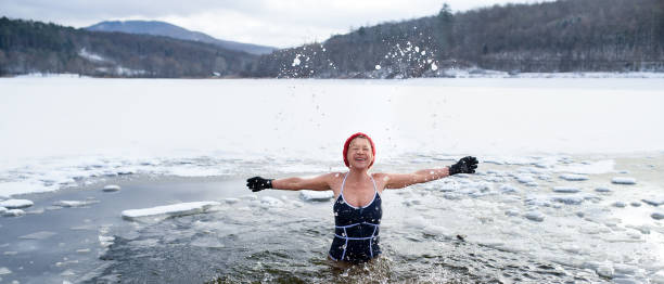 Front view of active senior woman in swimsuit outdoors in water in winter, cold therapy concept. A front view of active senior woman in swimsuit outdoors in water in winter, cold therapy concept. woman cold water swimming stock pictures, royalty-free photos & images