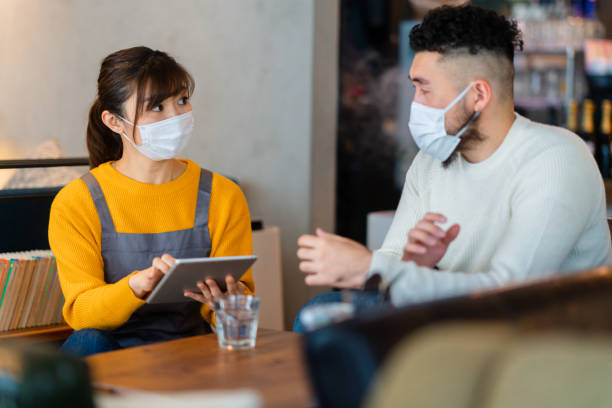 istock Waitress with protective face mask taking orders with digital tablet from customer 1300847047