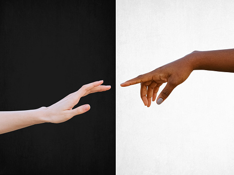 Friendship and racial respect concept with black and white hands reaching towards each other on black and white background