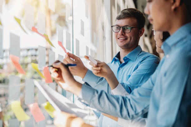 istock Group of young modern business people planning and brainstorming putting sticky notes on glass wall in the office. 1300848549