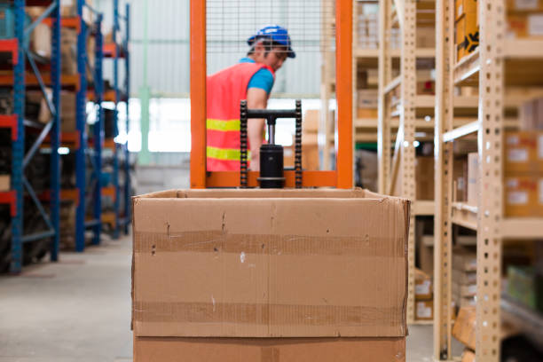 Asian male warehouse worker in safety vest and helmet driving and operating on forklift truck in the industry storage warehouse with shelf pallet automotive spare parts parcel blur background trabajador de almacén masculino asiático con chaleco de seguridad y casco conduciendo y operando en carretilla elevadora en el almacén de almacenamiento de la industria con paquete de piezas de repuesto automovilísticas de palets de estante de fondo bo
