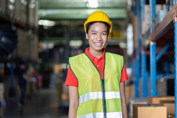 verticale de l’ouvrier noir de sourire d’entrepôt féminin au travail dans l’entrepôt de stockage d’industrie. femme afro-américain dans le gilet et le casque de sécurité à l’entrepôt d’étagère d’étagère - red vest photos et images de collection