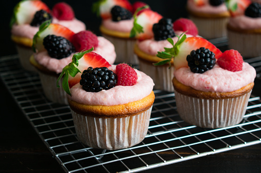 Cupcakes decorated with pink frosting and fresh berries on wire cooling racks