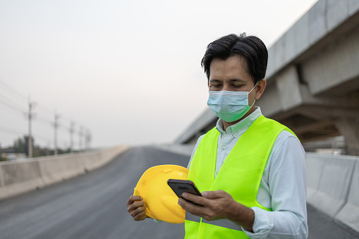 Portrait engineer working on his smartphone and wearing protective face mask at the construction site