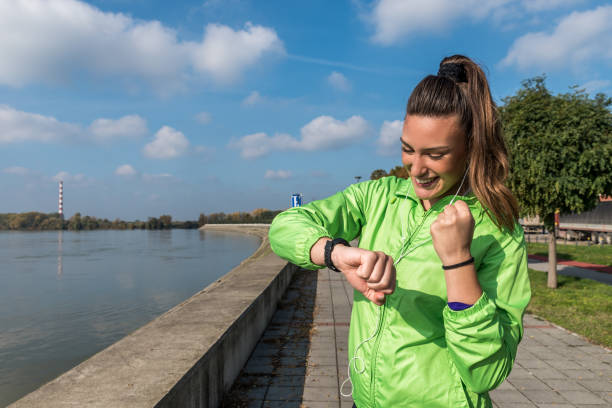 junge aktive schöne schöne sportliche fitness frau oder mädchen überprüfen ihre zeit auf ihrer armbanduhr nach outdoor-training und eine pause vom joggen und laufen - checking the time watch women looking stock-fotos und bilder