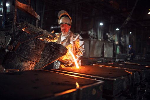 Trabajador de fundición vertiendo hierro fundido en moldes para la producción de acero. Industria pesada y proceso de metalurgia. photo