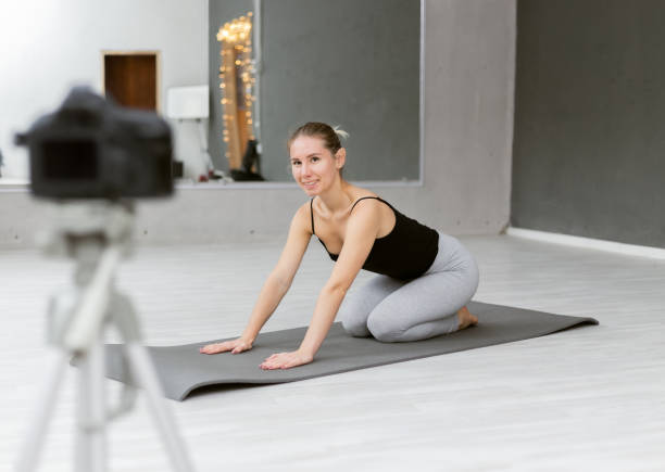 istock Fit woman yoga coach indoor records vlogs, using camera on tripod. Online learning concept, online classes 1300859596