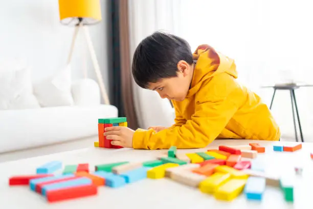 Little cute kid is playing colorful wooden blocks game  home in the living room.  Having fun and learning creativity.