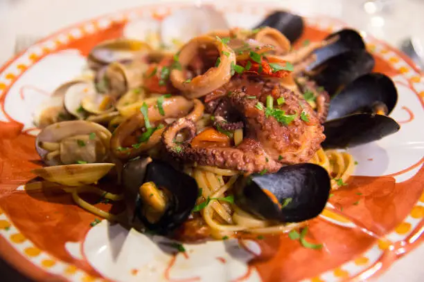 Italian food: seafood spagetti with grilled octopus and mussels on a hand-painted ceramic plate of the island of Capri, Tyrrhenian sea, Italy