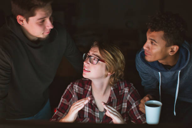 istock Group of young computer nerds gathered around a glowing screen at night 1300865544