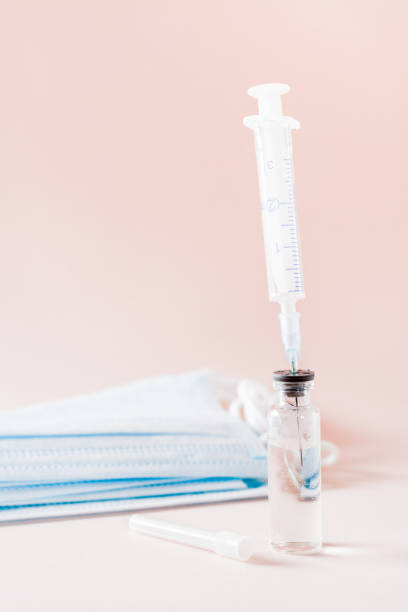 istock Vaccination and Immunization. Syringe needle inserted into glass vaccine vial and face mask. Vertical view 1300865692