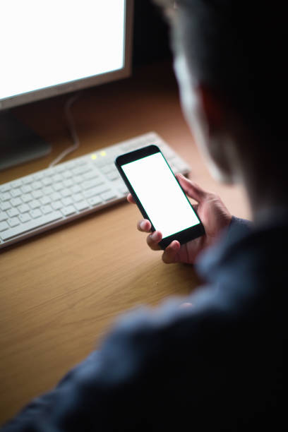 Young man multitasks with his cellphone in front of his desktop computer