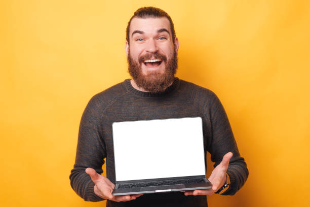 istock Amazed handsome bearded man showing white screen on laptop and smiling 1300869688