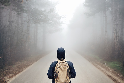 A teenager is walking on a road in the mist.