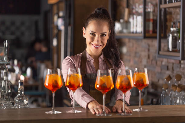 istock Beautiful bartender serves five orange cocktails in wine glasses on a bar. 1300871045