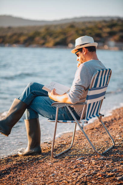 istock Young Man Reading a Book on the Beach 1300878424