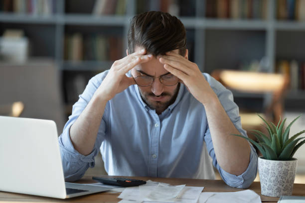 Frustrated young man feeling stressed calculating earnings or domestic expenses.
