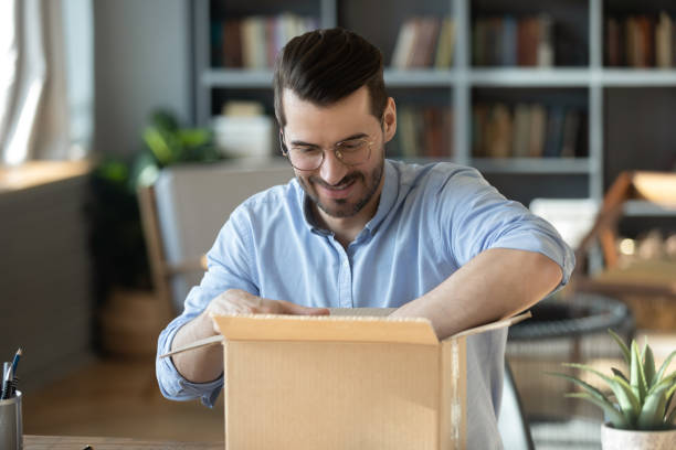 istock Curious young man in eyeglasses unpacking huge cardboard box. 1300879296
