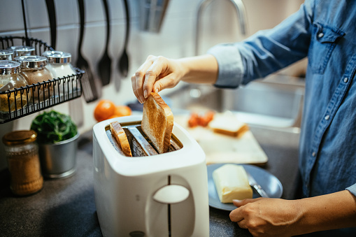 Woman using toaster to prepare breakfast at home
