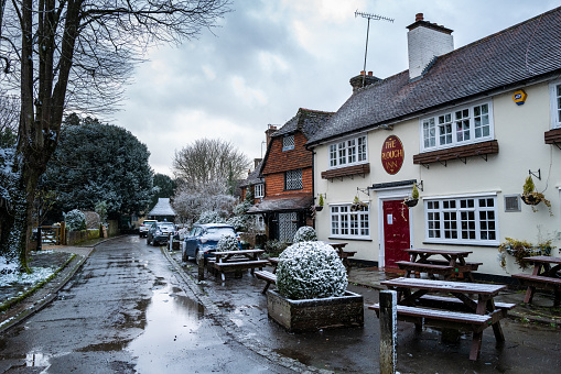 Ifield, UK - 7 February, 2021: color image depicting a quaint, traditional country pub in the old village of Ifield, near Crawley, in the south of England. It is winter and there is a dusting of snow on the ground and on the parked cars.