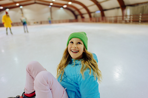 Photo of a smiling girl who fell down while ice-skating on an ice rink.