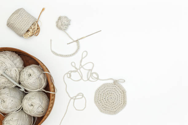 Skeins of gray cotton yarn in a wicker basket and accessories made from these threads. On a light background, with space, top view stock photo