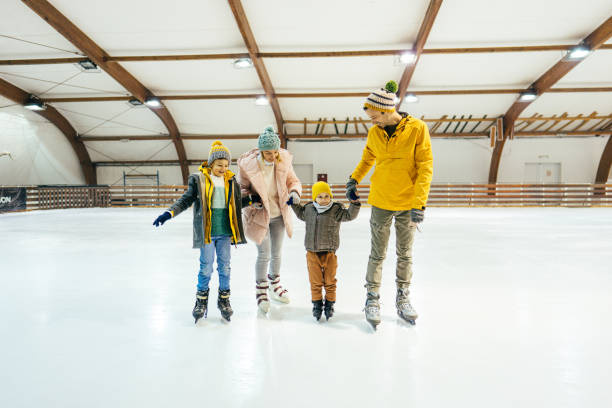 Family ice-skating Photo of two boys learning how to ice-skate on the ice rink, while their parents are holding their hands and showing them some basic steps and tricks. ice skating photos stock pictures, royalty-free photos & images