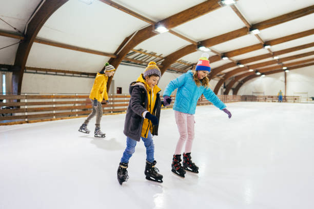 Ice-skating with my sister Photo of a little boy learning how to ice-skate on the ice rink, while his sister is holding his hand and guiding him. skate rink stock pictures, royalty-free photos & images