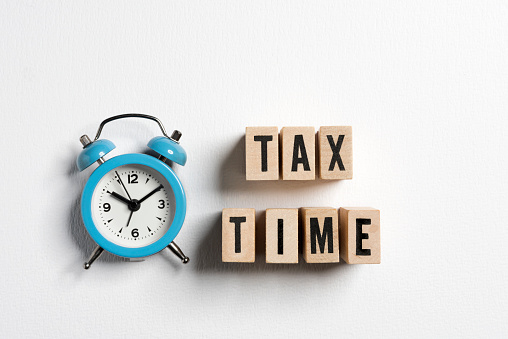 The word tax time written on wooden cubes with an alarm clock on white background. Tax payment reminder or annual taxation concept.