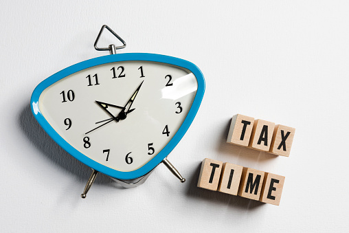 The word tax time written on wooden cubes with an alarm clock on white background. Tax payment reminder or annual taxation concept.