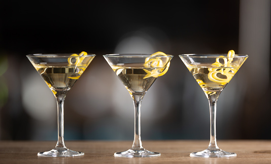 Dry martini with lemon peel and green olives on a black background.