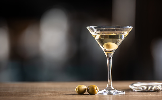 glass with brown alcoholic drink and piece of ice stands on the bar. Blurred view of restaurant in background.