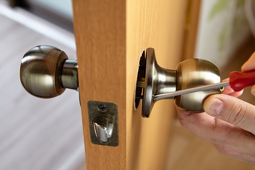 Locksmith fixes door handle rose with screw, using  screwdriver.