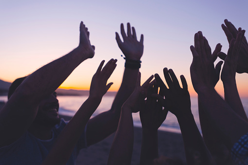 Silueta de un grupo de personas con las manos levantadas al atardecer o al amanecer. photo