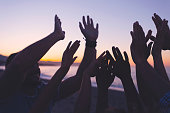 Silhouette of a Group of people with their hands raised at sunset or sunrise.