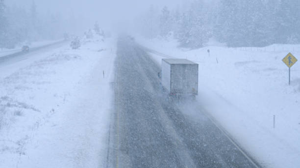 Trucks and cars make their way through a blizzard along a dangerous country road Cargo trucks and cars make their way through an intense blizzard along a dangerous country road leading through pine woods in Washington. Stunning shot of traffic moving through a bad snowstorm. blizzard stock pictures, royalty-free photos & images