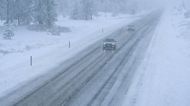 istock Two cars navigate along an icy road leading through forest caught in a blizzard. 1300896277