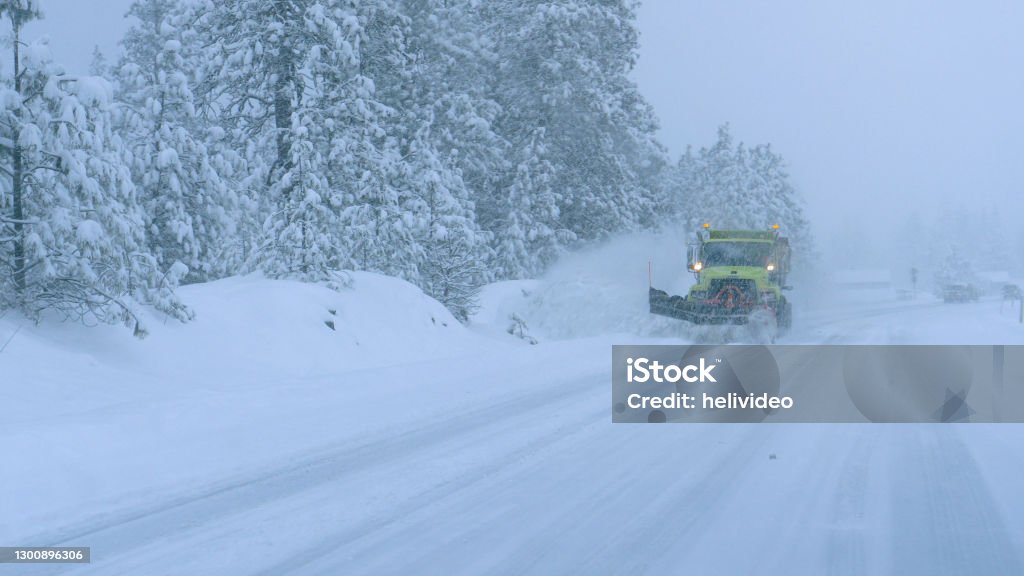 CLOSE UP: Truck plows the snowy country road during a horrible snowstorm. CLOSE UP: Truck plows the snowy country road during a horrible snowstorm raging in the state of Washington. Cars carefully drive behind a snow plough clearing the road during a devastating blizzard. Blizzard Stock Photo