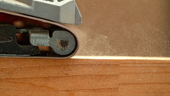 MACRO, DOF: Industrial sanding machine smooths out at wooden board sitting on the carpenter's workbench. Detailed shot of coarse sandpaper finishing up a carpenter's workpiece. Carpentry process.